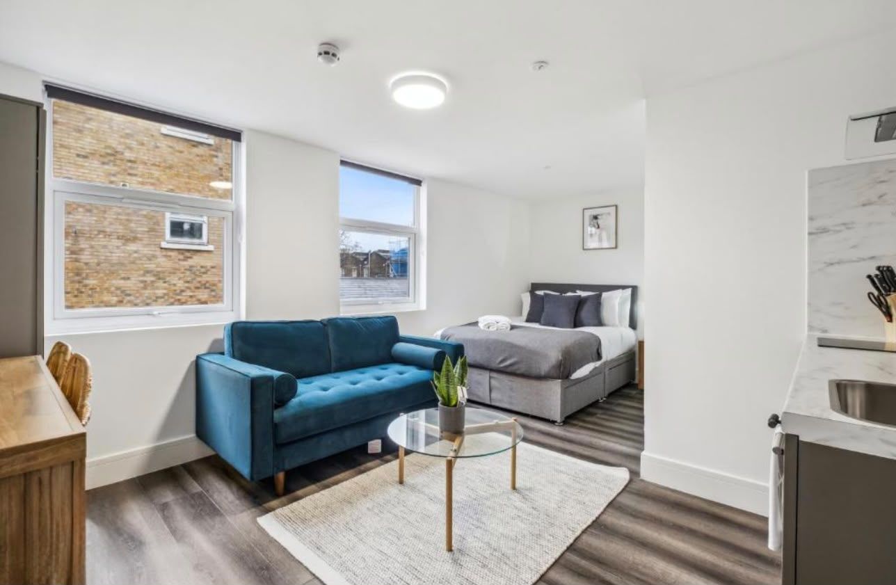 Studio with teal sofa, bed and two windows