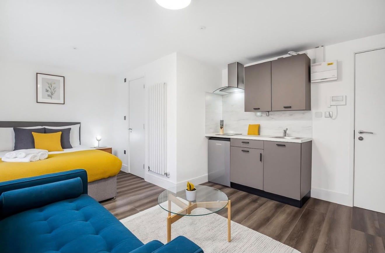 Studio with a yellow bed throw, sofa and kitchen