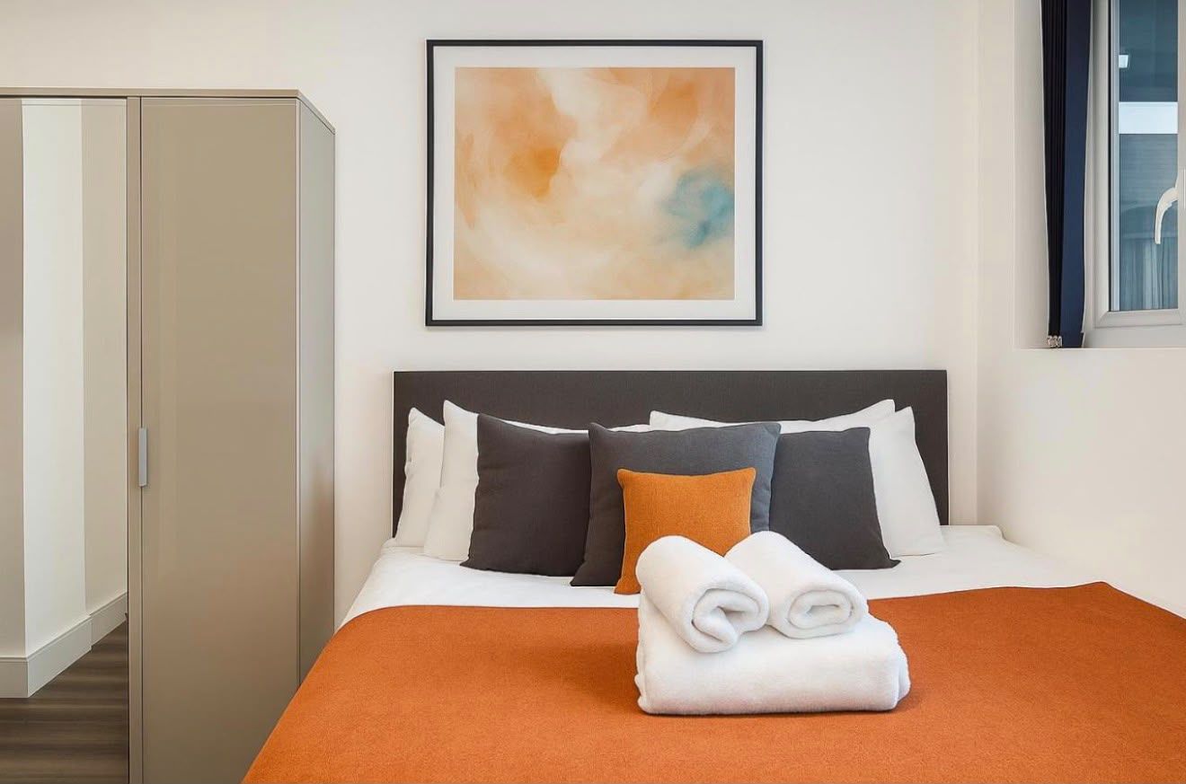 Bed with an orange throw and framed abstract print