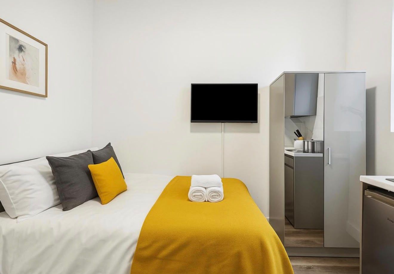 Compact studio with a yellow bed throw and wall-mounted television