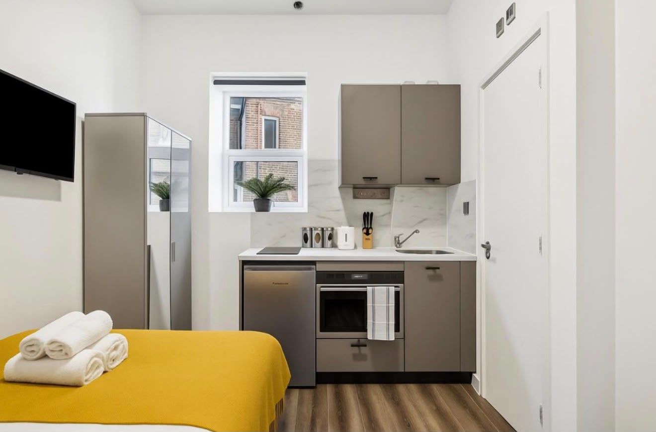 Kitchenette beside a bed with a yellow throw
