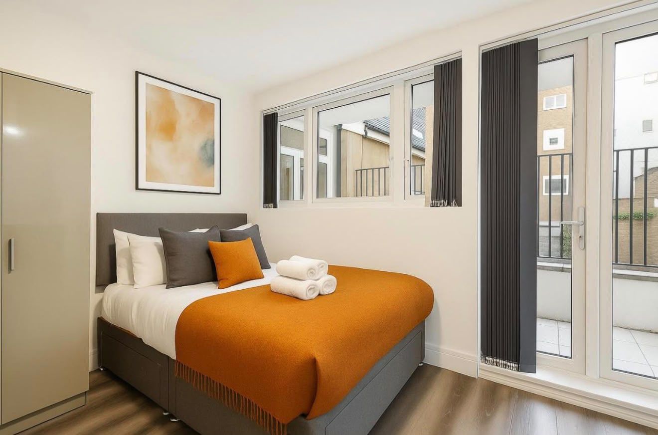 Bed with an orange throw beside french doors to a balcony