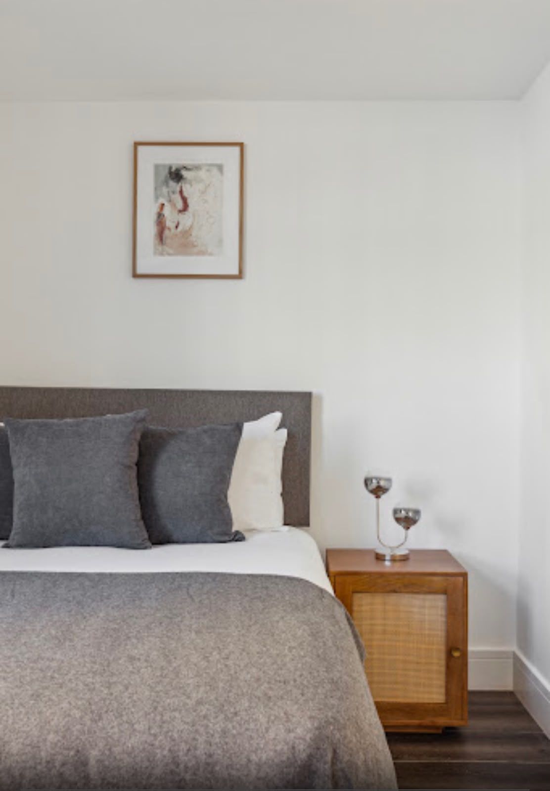 Bed with grey linen and a framed print above the headboard